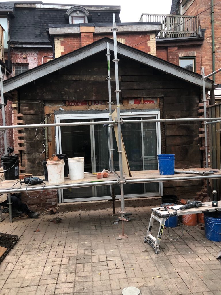 Bricks have been removed and the wooden framing is exposed on this 19th century wall at the rear of a row house. Scaffolding is setup in front of the wall.